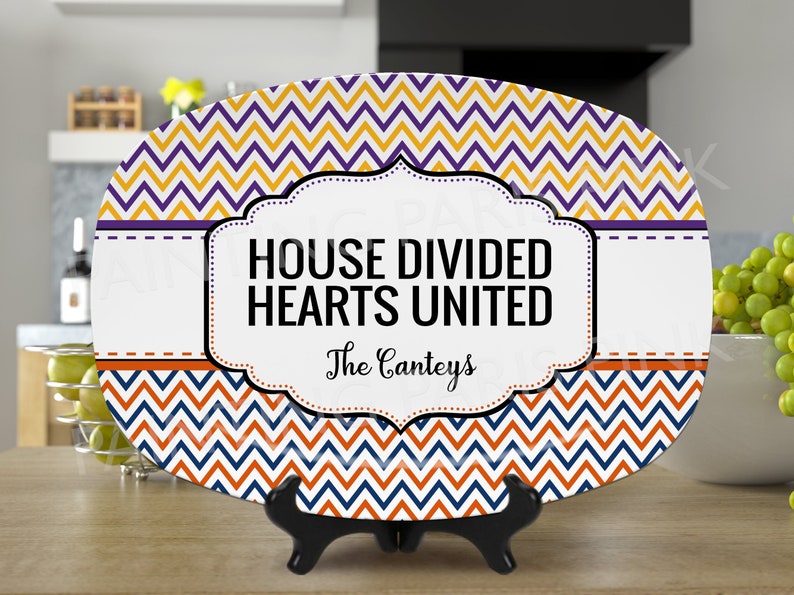 Może przedstawiać: Biała owalna tacka do serwowania z wzorem chevron w kolorze pomarańczowym, niebieskim i ż&oacute;łtym. Taca ma ozdobną ramkę z tekstem "House Divided Hearts United" i "The Canteys".