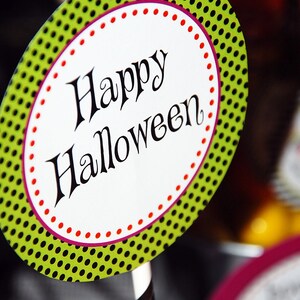 Pode incluir: Decoração de Halloween com um oval branco com a inscrição "Happy Halloween" em escrita preta. O oval é contornado por pontos vermelhos e um padrão de bolinhas verdes. Uma palhinha listrada a preto e branco é visível.