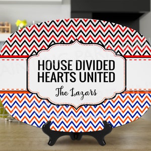 Może przedstawiać: Biały owalny talerz do serwowania z wzorem w czerwono-czarno-niebieskie chevron. Talerz ma czarną i białą ramkę z tekstem "HOUSE DIVIDED HEARTS UNITED" i "The Lazars".