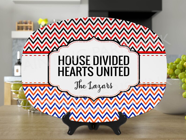 Może przedstawiać: Biały owalny talerz do serwowania z wzorem w czerwono-czarno-niebieskie chevron. Talerz ma czarną i białą ramkę z tekstem "HOUSE DIVIDED HEARTS UNITED" i "The Lazars".