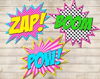 May include: Three colorful superhero-themed photo booth signs with the words "ZAP!" "BOOM!" and "POW!" printed on them. The signs are designed to look like comic book speech bubbles.