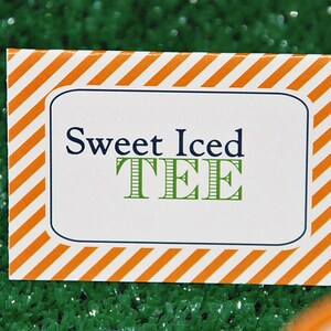 May include: A rectangular sign with a white background and orange diagonal stripes around the border. The sign has a blue border and the words "Sweet Iced TEE" in navy blue and green.