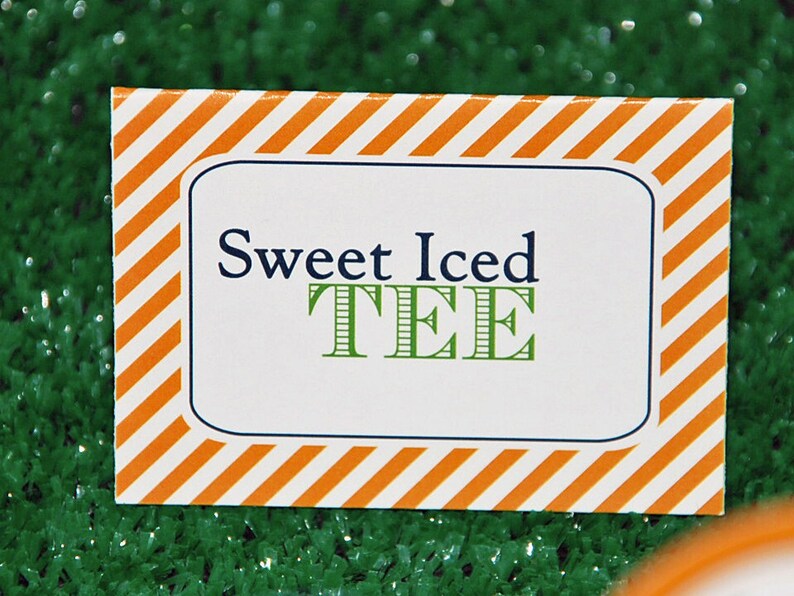 May include: A rectangular sign with a white background and orange diagonal stripes around the border. The sign has a blue border and the words "Sweet Iced TEE" in navy blue and green.