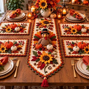 Op de afbeelding: Een tafelset met een gehaakte loper met een centrale kalkoenfiguur, zonnebloemen en pompoenen. Vier bijpassende rechthoekige placemats tonen soortgelijke herfstmotieven. Servetten zijn vastgezet met zonnebloemringen op witte borden.