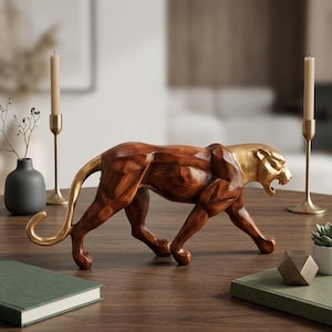 May include: A sculptural figurine of a prowling panther featuring a polished gold head and tail contrasted with a dark brown, faceted wooden-textured body. The animal is depicted in a mid-stride position with its mouth open, showcasing sharp teeth.