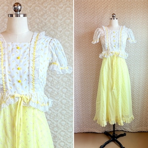 May include: A vintage-style dress with a white bodice and a yellow skirt. The bodice features yellow buttons, lace trim, and short sleeves. The skirt is a light yellow with a subtle floral pattern, and a ruffled hem. The dress is displayed on a mannequin.