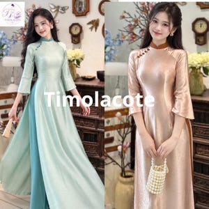 Puede incluir: Dos vestidos de manga larga con cuello alto y aberturas laterales. El vestido de la izquierda es verde claro con una capa inferior azul verdoso, y el de la derecha es oro rosa metálico con cuello marrón. Ambos tienen botones laterales y el texto Timolacote.