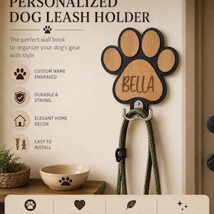 Peut inclure: Un porte-laisse pour chien mural en forme de patte, composé d'un cadre noir avec des inserts en bois clair. Le centre est gravé du nom BELLA. Un crochet double en métal argenté est fixé en bas, supportant une laisse de couleur verte.