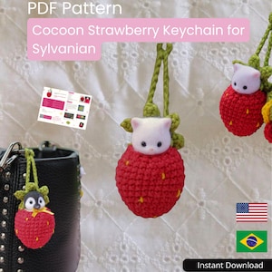 May include: A PDF pattern for a crochet cocoon strawberry keychain for Sylvanian figures. The design features a red strawberry with yellow seeds and green leaves, housing a small white cat or penguin figure, complete with a green hanging loop.