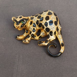 Op de afbeelding: Een broche van goudkleurig metaal in de vorm van een luipaard met zwarte vlekken en strass. De luipaard heeft groene ogen.