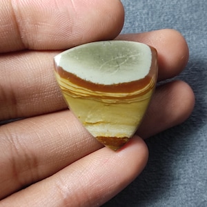 May include: A triangular polished gemstone featuring horizontal bands of color including a muted sage green top section, a deep reddish-brown middle layer, and a light mustard yellow base with subtle cream-colored striations throughout the stone.