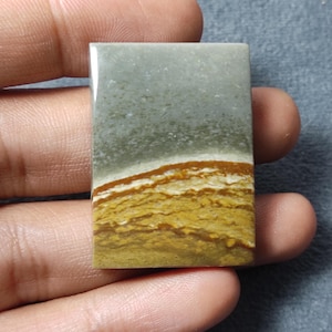 May include: A rectangular polished gemstone cabochon featuring a smooth surface with distinct color bands. The top section is a muted sage green, transitioning into a sharp white line, followed by layered horizontal bands of golden yellow and brown.