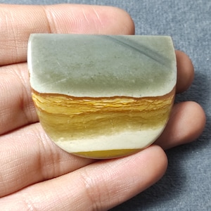 May include: A semi-circular polished stone cabochon featuring horizontal bands of color. The top section is a muted sage green, transitioning into layered stripes of golden yellow, ochre, and cream white at the rounded base of the stone.