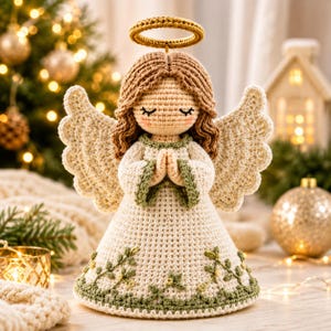 Peut inclure: Une figurine d'ange au crochet avec des cheveux en laine brun clair, une auréole dorée et des ailes crème. L'ange porte une robe crème avec une bordure verte et un motif de vigne brodé vert sur l'ourlet, les mains jointes en prière.