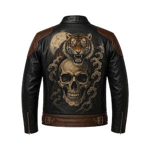 Puede incluir: Una chaqueta de cuero negro con paneles de cuero marrón en los hombros y un cinturón marrón con hebillas. La espalda muestra un estampado gráfico detallado de un tigre rugiendo sobre un cráneo humano, con una luna circular de fondo.