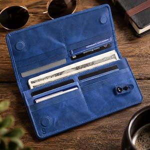 May include: A blue bifold wallet featuring multiple interior card slots, a long compartment for paper currency, and a small snap-button closure tab. The wallet has a matte finish and includes embossed circular details on the interior surface.