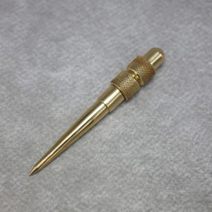 Könnte beinhalten: Eine goldfarbene Metallahle mit einer glatten, spitz zulaufenden Spitze und einem zylindrischen Griff, der zwei Abschnitte mit texturierter Kreuzrändelung für besseren Halt aufweist. Das Werkzeug hat durchgehend eine polierte, reflektierende Oberfläche.