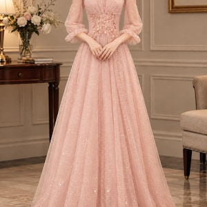 May include: A floor-length dusty pink gown featuring long sheer sleeves with ruffled cuffs, a square neckline, and a fitted bodice adorned with intricate floral embroidery. The skirt is made of a shimmering, glitter-infused tulle fabric.