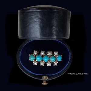 May include: A turquoise and pearl ring in a blue velvet ring box. The ring is made of gold and features a row of turquoise stones with pearl accents.