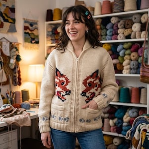 May include: A cream-colored knit zip-up cardigan featuring a prominent fox face design on the front panels, two front pockets, and a ribbed collar. The sleeves and hem are decorated with small paw print patterns in a contrasting dark color.