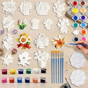 Pode incluir: Um kit de artesanato com várias formas de flores em gesso branco, algumas parcialmente pintadas com cores vivas. Inclui uma tira de potes de tinta, duas paletas em forma de flor, seis pincéis de cabo azul e ferragens para montagem.