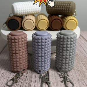 May include: A collection of cylindrical silicone keychains featuring a textured pyramid stud pattern. The keychains come in various colors including white, brown, black, tan, yellow, mauve, lavender, and gray, each with a metal lobster clasp.