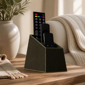 May include: A dark olive green desk organizer with a trapezoidal shape and a vertical ribbed texture on the exterior. The organizer features four internal compartments arranged in a stepped, slanted design to hold various office supplies.