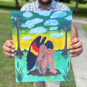 May include: A rectangular painting on paper depicting a figure with dark skin and black hair sitting in a fetal position on a small island. The figure has large wings with black, red, and yellow feathers. The background shows a swamp with trees, water, and a yellow sky with blue clouds.
