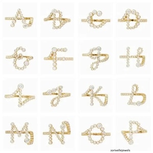 Könnte beinhalten: Eine Sammlung von sechzehn goldfarbenen Ringen, von denen jeder einen Buchstaben des Alphabets zeigt, der aus kleinen, runden, klaren Steinen in einer durchgehenden Linie besteht. Die Buchstaben A bis P sind in einem Raster angeordnet.