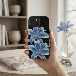 Puede incluir: Una funda de smartphone negra con un estampado gráfico de dos lirios azules con estambres amarillos y motas oscuras. El diseño cubre la parte posterior de la funda, mostrando los pétalos detallados de los lirios sobre un fondo negro sólido.