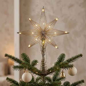 Könnte beinhalten: Ein silberner Drahtstern als Baumspitze mit einem vielzackigen Design und integrierten warmweißen LED-Lichtern. Der Stern ist auf einer spiralförmigen Drahtbasis befestigt, die auf einem grünen Tannenbaum sitzt, ergänzt durch zwei weiße Kugeln.
