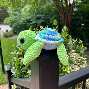 Peut inclure: Une peluche tortue au crochet avec une tête et des nageoires vert citron vif en fil texturé. La carapace présente un motif varié de fils bleu, turquoise et blanc. La tortue possède de grands yeux ronds et sombres avec des iris bleus.