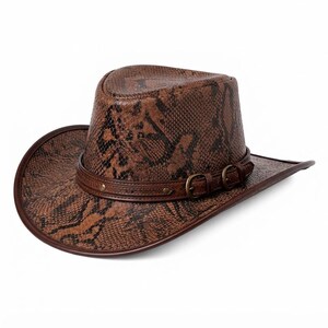 Könnte beinhalten: Ein brauner Cowboyhut mit einer strukturierten Schlangenhaut-Optik auf der Krone und der Krempe. Der Hut verfügt über ein dunkelbraunes Lederband um die Basis, das mit zwei kleinen messingfarbenen Schnallen und Metallnieten verziert ist.