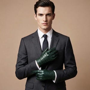 Peut inclure: Une paire de gants en cuir vert foncé avec un motif texturé en peau de crocodile. Les gants sont portés avec une veste de costume gris anthracite, une chemise blanche à col rigide et une cravate noire unie, créant une allure formelle.