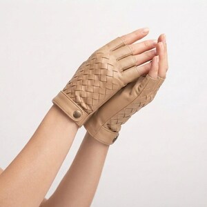 May include: A pair of fingerless gloves in a light tan color, featuring a woven leather pattern on the back of the hand and a smooth leather cuff with a small metallic snap button closure at the wrist for a secure fit.