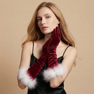 May include: A pair of long, deep red velvet gloves featuring white faux fur trim at the cuffs. The gloves extend past the wrists, showcasing a smooth, soft texture and a rich, dark crimson color that contrasts with the fluffy white feather-like trim.