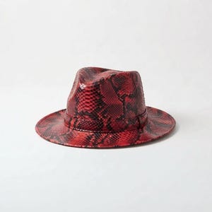 Peut inclure: Un chapeau fedora présentant un motif peau de serpent rouge et noir vif sur toute la surface. Le chapeau comprend une calotte structurée avec un pli central et une bande assortie en peau de serpent rouge et noire entourant la base.
