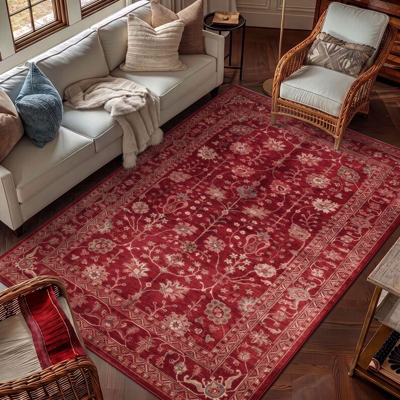 May include: A large rectangular area rug featuring a deep red background with an intricate floral and vine pattern in shades of cream, light pink, and muted blue, finished with a detailed decorative border along all four edges.