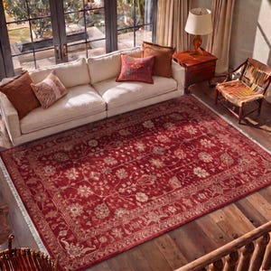 May include: A large rectangular area rug featuring a deep red background with intricate floral and vine patterns in cream, tan, and muted green tones. The rug has a wide decorative border and short white fringe along the two shorter ends.