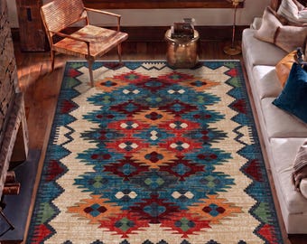 May include: A rectangular area rug featuring a cream-colored background with a central geometric pattern in shades of deep red, bright orange, and vibrant blue, bordered by a zigzag design in green, blue, and red with short fringe.