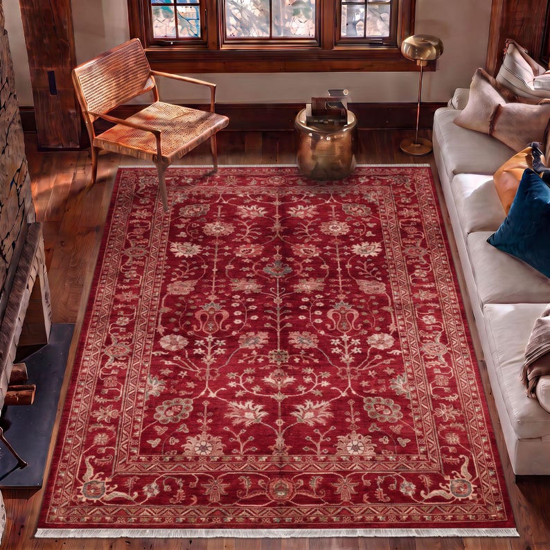 May include: A rectangular area rug featuring a deep red background with an intricate floral pattern in shades of cream, beige, and muted blue. The rug has a wide decorative border and short white fringe along the top and bottom edges.