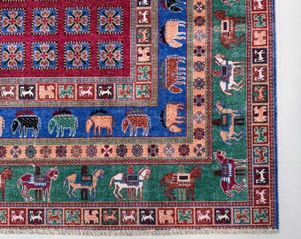 May include: A rectangular area rug featuring a deep magenta center with a grid of blue floral squares. The border displays rows of stylized horses and geometric patterns in shades of blue, green, red, and orange with a fringed edge.