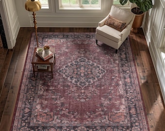 May include: A large rectangular area rug featuring a deep burgundy and muted charcoal gray color palette with a central floral medallion and an intricate border pattern, laid flat on a dark wood floor in a room with a chair and side table.