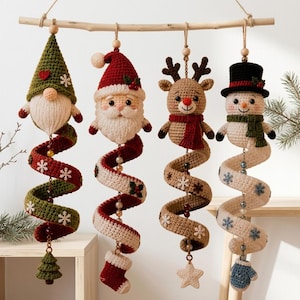 May include: Four hanging crochet Christmas ornaments suspended from a wooden branch. The figures include a green gnome, Santa Claus, a reindeer, and a snowman. Each character features a long, spiraling crochet tail decorated with beads and motifs.