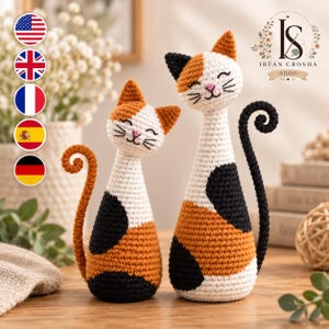 Könnte beinhalten: Zwei handgefertigte Häkel-Katzenfiguren mit einem Kaliko-Muster aus weißem, orangefarbenem und schwarzem Garn. Jede Katze hat eine gestickte rosa Nase, geschlossene Augen und einen langen, geringelten Schwanz. Die kleinere Katze hat einen orangen Schwanz, die größere einen schwarzen.