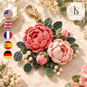 May include: A crochet keyring featuring two large, layered pink and light pink peony-style flowers, two smaller closed buds, and several dark green leaves with small white berries, all attached to a gold-toned metal lobster clasp.