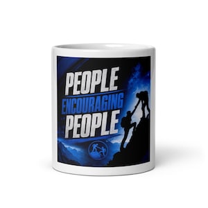 Puede incluir: Una taza de cerámica blanca con un diseño gráfico en azul y negro. El texto PEOPLE ENCOURAGING PEOPLE aparece en letras blancas y azules. La imagen muestra la silueta de dos personas escalando una montaña y ayudándose mutuamente.