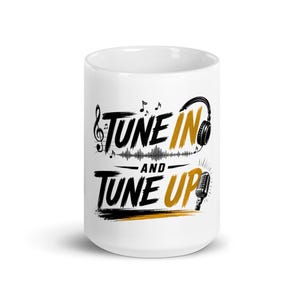 Puede incluir: Una taza de cerámica blanca con texto gráfico en negro y dorado que dice TUNE IN AND TUNE UP. El diseño incluye ilustraciones de notas musicales, un patrón de ondas sonoras, auriculares y un micrófono de estilo vintage.