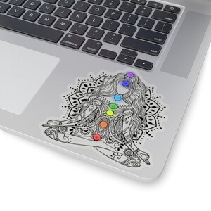 May include: A black and white illustration of a woman sitting in a yoga pose with a mandala behind her. The woman has seven chakras represented by colored circles on her body.