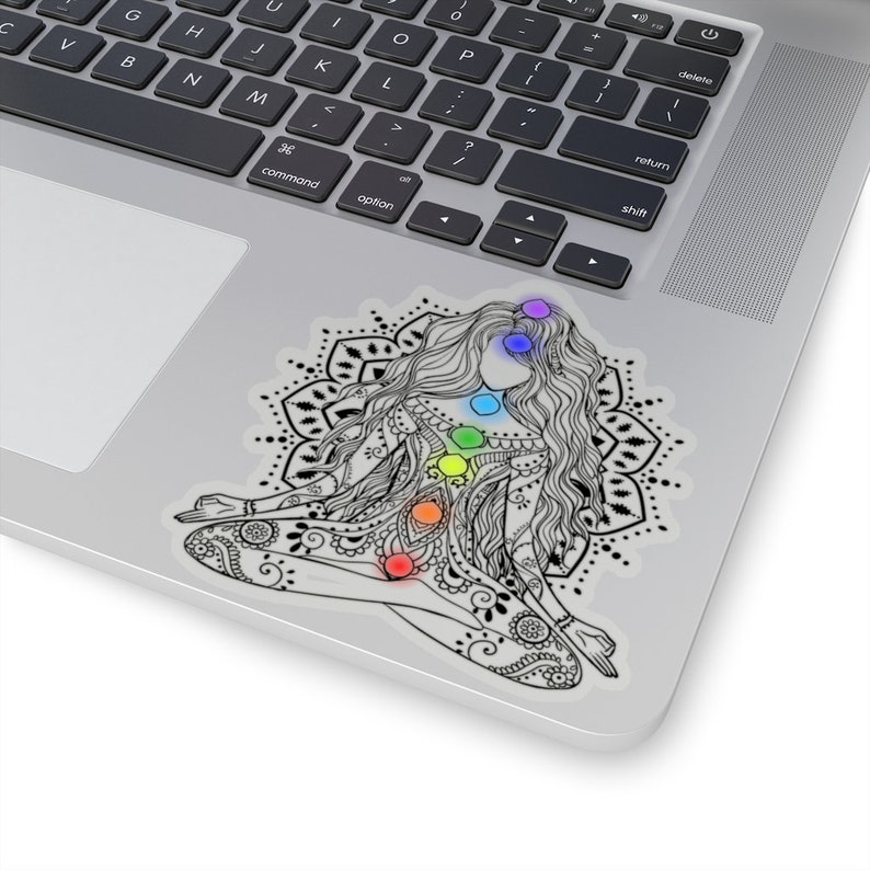 May include: A black and white illustration of a woman sitting in a yoga pose with a mandala behind her. The woman has seven chakras represented by colored circles on her body.